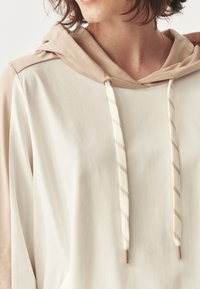 Sudadera con capucha en crema y beige, que presenta paneles en contraste, cordones texturizados con rayas y un ajuste relajado.