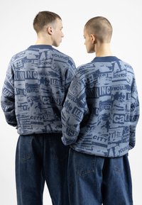 Kék mintás pulóverek szöveges grafikákkal, kerek nyakkal és oversized fazonnal, laza kék farmernadrággal párosítva.