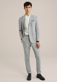 Traje gris a rayas con un ajuste a medida, combinado con una camiseta polo de color claro. Presenta botones de acento marrón y zapatos negros.