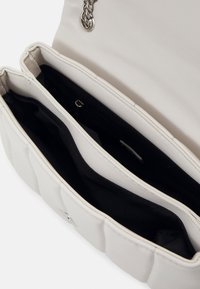 Sac à bandoulière en cuir blanc avec une lanière chaîne argentée, ouvert montrant deux compartiments principaux doublés de tissu noir.