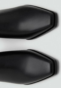 Stivali in pelle nera alla caviglia con punta affusolata, texture liscia e una leggera lucentezza. Il design include un tacco basso e linee pulite.