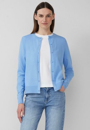 Lichtblauwe cardigan van gebreide stof, met een ronde halslijn, knopen aan de voorkant en geribbelde manchetten. Gecombineerd met een wit T-shirt en blauwe spijkerbroek.