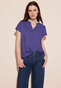 Blusa viola a maniche corte con scollatura a V. Il tessuto è morbido e leggero. Abbinata a jeans a gamba larga blu scuro. Design semplice e moderno.