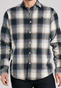 Mężczyzna w koszuli w kratę z długim rękawem w niebieskie, białe i brązowe kolory, zapiętej na guziki, na neutralnym szarym tle.