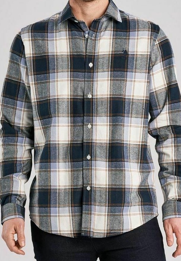 Mężczyzna w koszuli w kratę z długim rękawem w niebieskie, białe i brązowe kolory, zapiętej na guziki, na neutralnym szarym tle.