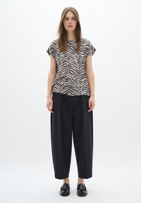 Top a maniche corte morbido con un motivo a strisce zebra nero e beige, abbinato a pantaloni neri larghi e scarpe nere lucide.