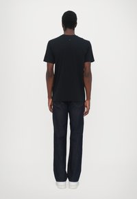 Camiseta de algodón negra con cuello redondo, combinada con unos vaqueros rectos de tono azul oscuro y zapatillas blancas, vista desde la parte de atrás.