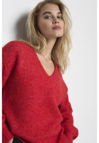 Roter Strickpullover mit V-Ausschnitt und lockerer Passform. Verfügt über strukturiertes Garn, lange Ärmel und gerippte Bündchen, die ein gemütliches Erscheinungsbild bieten.