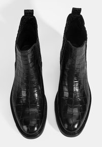 Bottines noires en cuir avec un motif crocodile texturé, bout rond, panneaux latéraux élastiques et languettes pour un enfilage facile.