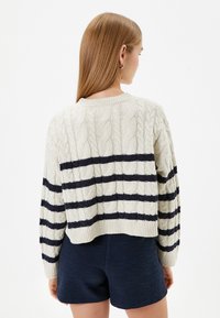 Crème kabelgebreide trui met marineblauwe strepen, ronde halslijn en cropped pasvorm. Textuurstof met ribbed mouwen en zoom.
