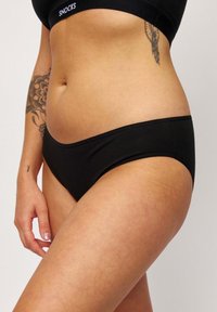 Zwarte katoenen bikini met een lage taille. Vloeiende textuur en naadloze randen voor comfort. Voorzien van een merkband van elastiek.