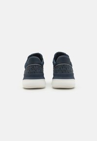 Adidași bleu marin din material texturat, cu un model de logo pronunțat, guler căptușit la gleznă și talpă din cauciuc alb.