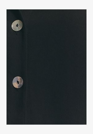 Schwarzer Stoff mit einem auffälligen runden Knopf in natürlicher Ausführung und einem einzelnen Loch, der eine glatte, strukturiert Oberfläche betont.