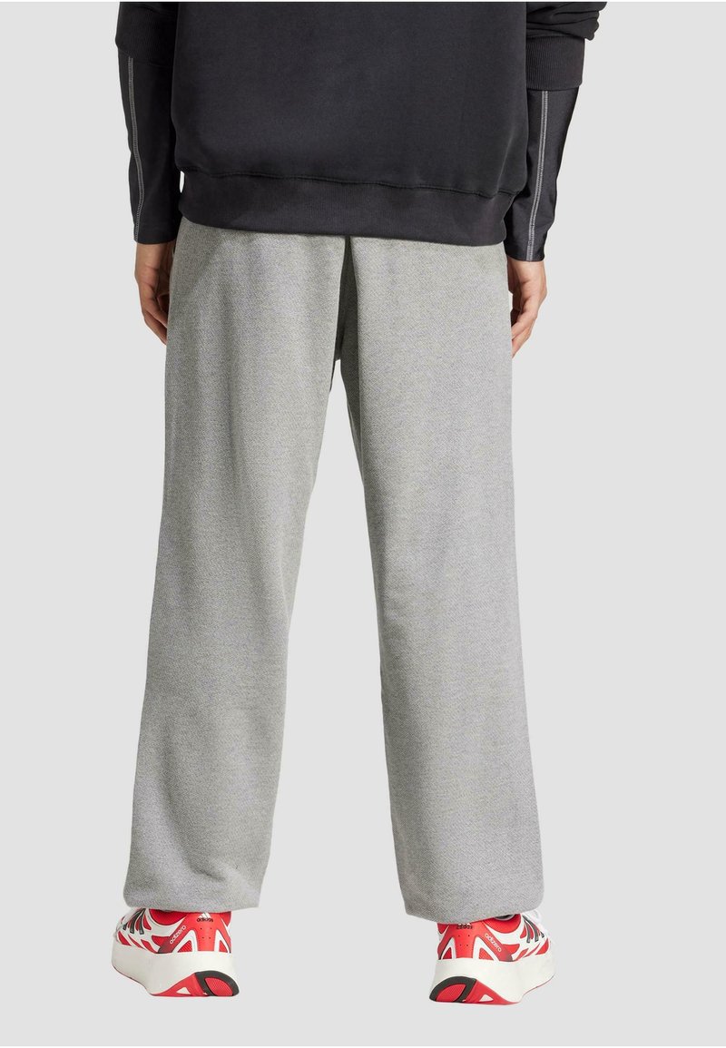 Pantalons de survêtement gris clair, à coupe décontractée, fabriqués dans un tissu doux, présentant une texture simple et associés à des chaussures accentuées de rouge.