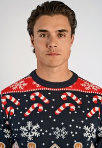 Stickad jultröja i marinblått med röda accenter. Har mönster med godiskäppar, snöflingor och pepparkakshus. Ribbad krage.