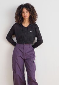 Black cropped hoodie with a front zipper and a small logo, paired with purple cargo pants featuring side pockets and stitch detailing.