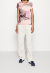 Kortärmad, figursydd topp i rosa och grå blommönster. Kombinerad med crèmefärgade vida byxor och marinblå sneakers med blåa ränder.