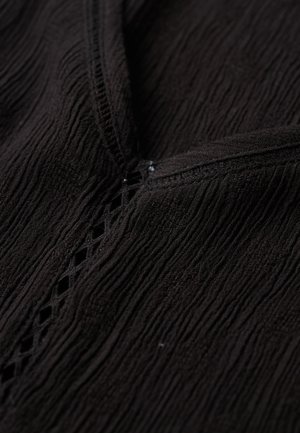 Primer plano de tela negra texturizada con patrón arrugado y detalle decorativo de cortes en forma de rombo a lo largo de una costura.