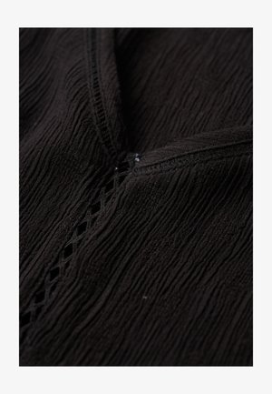 Primer plano de tela negra texturizada con patrón arrugado y detalle decorativo de cortes en forma de rombo a lo largo de una costura.