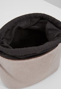 Okrągła torba wykonana z teksturowanego, jasnoróżowego materiału, z czarną podszewką z tkaniny i ściąganym górnym zamknięciem. Wewnątrz widoczna metka.