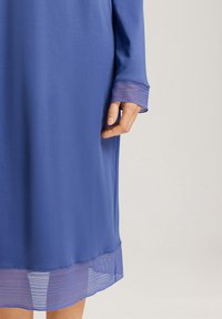 Vestito blu con maniche lunghe, caratterizzato da un bordo in pizzo trasparente sui polsini e sull'orlo, realizzato in tessuto morbido con una texture liscia.