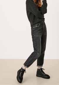 Zblakłe czarne jeansy o wysokim stanie z luźnym krojem, połączone z czarnymi sznurowanymi ciężkimi butami oraz fakturowanym czarnym swetrem.