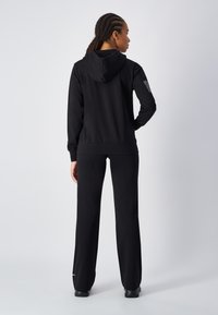 Sudadera con capucha negra y pantalones de chándal a juego, hechos de una tela suave. Presenta puños acanalados y un pequeño logo en la pierna del pantalón.