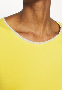Gelbes Baumwoll-T-Shirt mit Rundhalsausschnitt und hellgrauem Abschluss. Glatte Textur und einfaches Design ohne sichtbare Muster oder Grafiken.