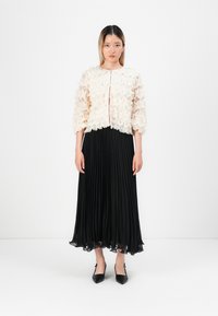 Blusa bianca a volant con maniche a tre quarti, abbinata a una gonna nera fluente a pieghe e tacchi neri a punta. Design minimalista.