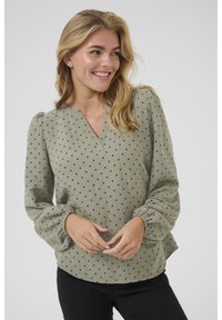 Lichtgroene blouse met zwarte stippen, v-hals en pofmouwen. Zachte, textuurstof met een relaxte pasvorm.