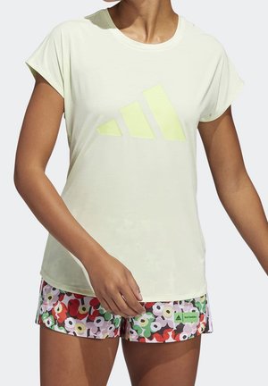 Ljusgul sportt-shirt med korta ärmar och en grönaktig-gul Adidas-logo. Matchas med blommönstrade shorts i olika färger.