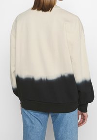 Felpa oversize in tinta unita crema e nera, con orlo e polsini a coste. Realizzata in morbido misto cotone, con una vestibilità comoda.
