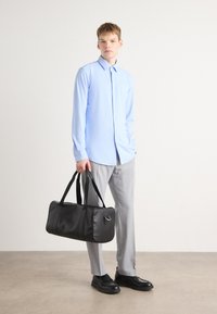 Camisa de manga larga azul claro, pantalones grises y zapatos de piel negros. Bolsa de deporte negra con textura suave y doble asa.