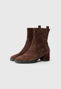 Botas de ante marrón hasta el tobillo con punta redonda, tacón cuadrado corto y paneles laterales, que cuentan con tiradores para facilitar su uso. Suela de goma para mayor tracción.