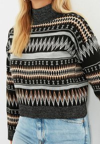 Schwarzer und gemusterter Pullover mit hohem Kragen, langen Ärmeln und geometrischen Designs in Weiß, Grau und Kupfer. Rippendetail am Saum.