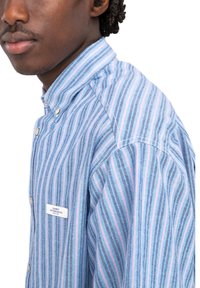 Camicia a righe in blu, rosa e navy. Caratterizzata da un colletto a punta e un piccolo logo sul petto. Tessuto leggero con una consistenza liscia.