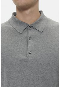 Grå pikétröja i mjukt tyg med krage och treknappsstängning. Texturen är slät med ett subtilt stickmönster.