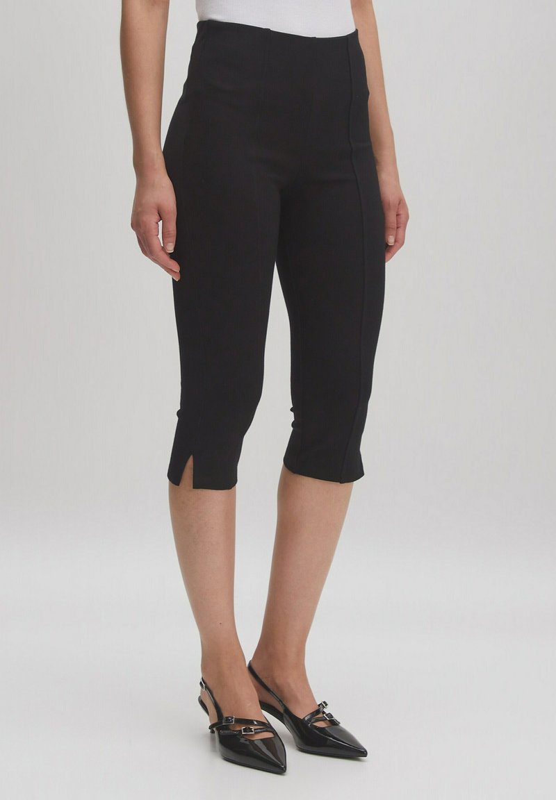 Zwarte cropped broek met een hoge taille en zijsplitten aan de zoom, gemaakt van een gladde stof, gecombineerd met zwarte puntige slingback schoenen.