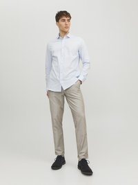 Chemise bleu clair à boutons, pantalon beige et chaussures noires. Présente un col standard et une texture lisse. Design et coupe minimalistes.