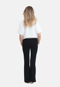 Vit kortärmad t-shirt med avslappnad passform, tillsammans med svarta utsvängda byxor. Slät tygtextur, visar bakvyn av outfiten.