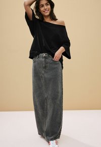 Černý svetr bez ramínek spárovaný s dlouhou šedou džínovou sukní. Sukně má rovný střih a viditelné švy. Modelka má na sobě bílé tenisky s červenými akcenty.