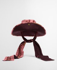 Breedgerande hoed van roze corduroy met een geruit patroon en een kastanjebruine sjaal die aan de basis is geknoopt. Heeft een ronde kroon en gouden accent.