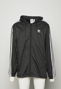 Černá bunda na zip s kapucí, bílé pruhy podél rukávů, elastické manžety a logo Adidas na hrudi. Hladká, lehká látka.