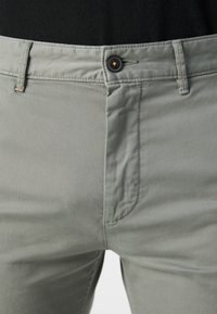 Pantaloni gri deschis din bumbac moale. Au închidere cu buton, buzunare frontale și detalii fine de cusătură pe cusături.
