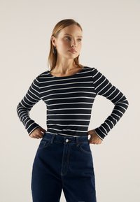 Langermet topp i marineblå med hvite horisontale striper, rund halsutskjæring og tettsittende design; kombinert med høyt liv mørk denimjeans.