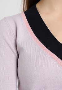 Hellblaues Sweatshirt mit V-Ausschnitt, ausgestattet mit einem schwarzen Kragen und pinken Akzenten. Weicher Stoff mit gerippten Details am Ausschnitt.