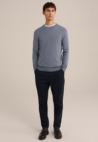 Suéter de manga larga azul claro combinado con pantalones oscuros de color navy y zapatos negros. El suéter tiene un cuello redondo y puños acanalados.