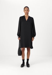 Črna obleka z dolgimi rokavi, vertikalnimi nagubanji in V-izrezom. Mehka, tekoča tkanina in čipkast rob na manžetah. V kombinaciji z črnimi nogavicami in čevlji.