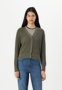 Olivovo zelený pletený sveter s výstrihom do V, sedem gombíkov na prednej strane, ribovaný povrch a priliehavé manžety, položený na pruhovanej košeli.