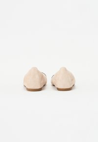 Bailarinas de ante en beige claro con punta redondeada y suela baja de goma marrón, que presentan una textura suave y un diseño minimalista.